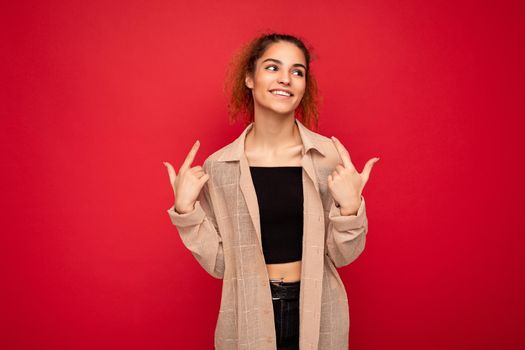 Photo of young positive smiling happy beautiful attractive brunette wavy-haired woman with sincere emotions wearing casual beige shirt isolated on red background with empty space.