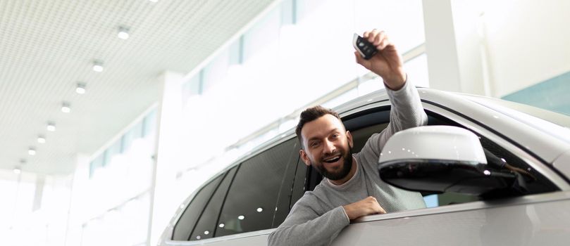 happy owner of a new car demonstrate car keys in a car dealership.