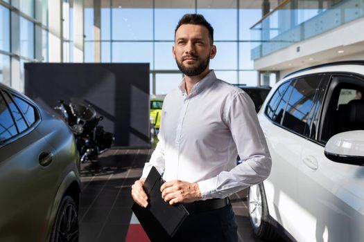 automobile center specialist against the backdrop of a car dealership with a folder in his hands.