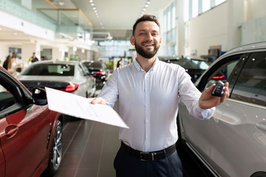 sales manager in a car dealership hands over the keys and documents to the car.