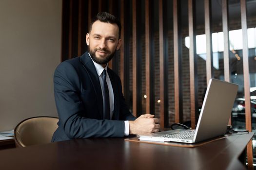 employee of the sales department at the workplace in a modern office sits at a laptop and looks at the camera.