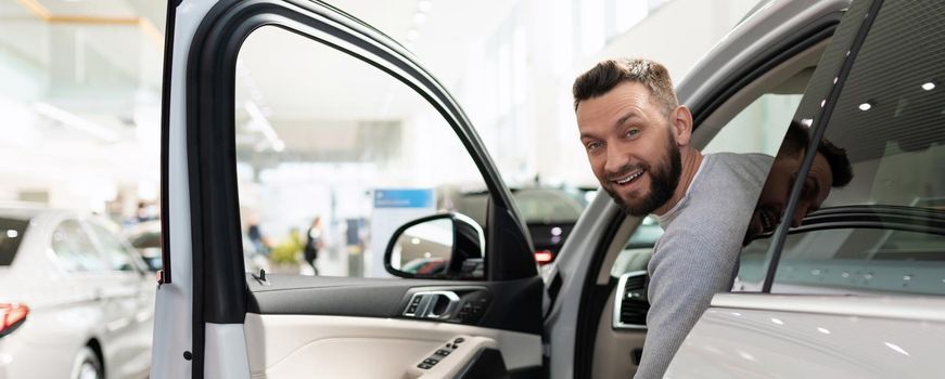 satisfied customer peeks out from behind the wheel of a new SUV at a car dealership.