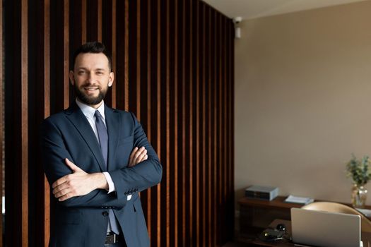 successful entrepreneur businessman in a strong office with his arms folded on his chest looks at the camera with a smile.