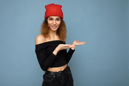 Portrait of beautiful fascinating emotional positive joyful happpy female promoter pointing to the side at copy space for advertising wearing hipster outfit isolated over background wall with empty space with sincere emotions.