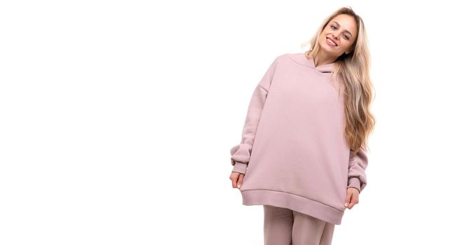 blonde with a smile on her face on a white background in a pink hoodie.