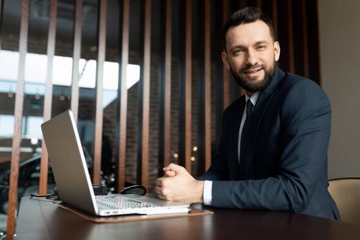 manager of an insurance company in the office sitting at a laptop looking with a smile.