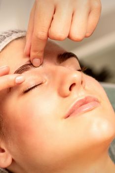 Eyebrow massage. Beautiful caucasian young white woman receiving an eye and eyebrow massage with closed eyes in a spa salon