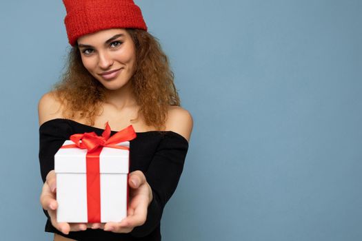 Shot of attractive positive smiling young woman isolated over colourful background wall wearing everyday trendy outfit holding gift box and looking at camera. Empty space