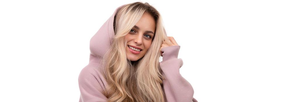 widescreen photo of a blonde with a smile on her face in a pink tracksuit and a hood