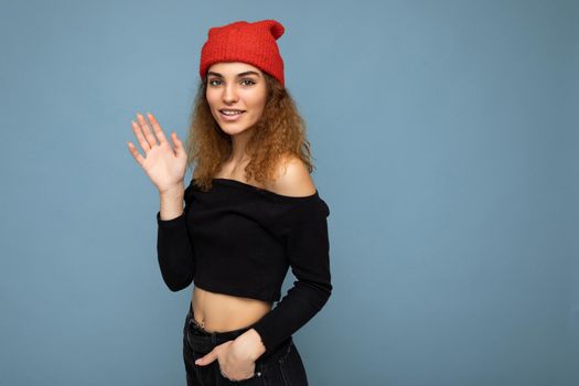 Photo of young positive happy smiling beautiful woman with sincere emotions wearing stylish clothes isolated over background with copy space and waving with hand. Hello concept.