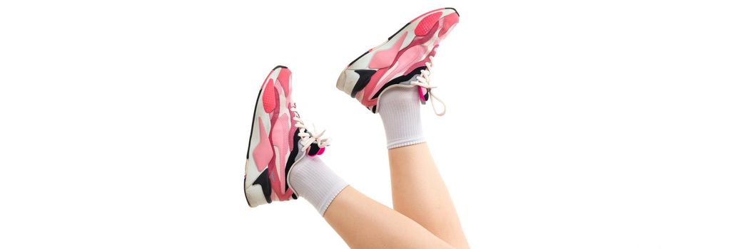 photo of female legs in pink sneakers on a white background.