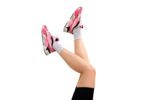 legs of a young woman in sneakers on a white background.