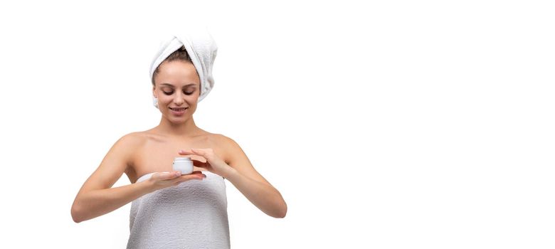 young woman after a shower on a white background with a jar of white cream in her hands.