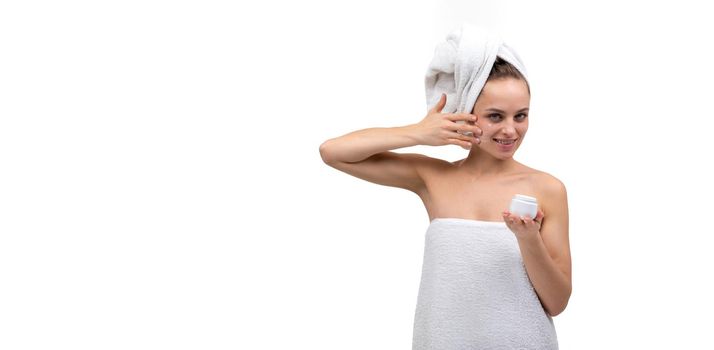 a woman after a shower on a white background applies a cream to her face.