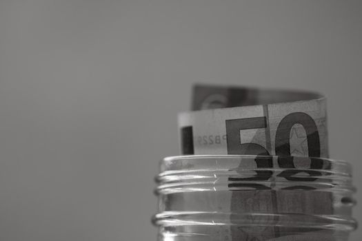 Composition with saving money banknotes (50 EURO) in a glass jar. Concept of investing and keeping money, close up isolated.