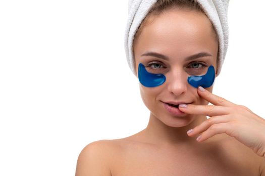 blonde after a shower with blue cosmetic patches on her face to care for the skin around her eyes looks sexy at the camera, holds her hand near her lips.