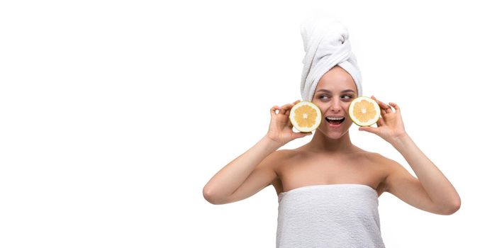 beautiful well-groomed young woman with a towel on her body after a shower with a smile looking at the camera holding oranges.