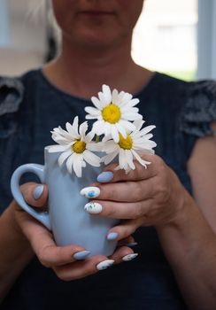 a young woman holds a blue cup of daisies, a beautiful summer manicure. High quality photo