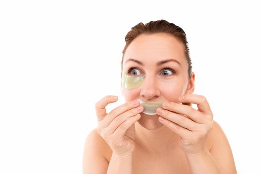 young woman grimacing playfully lowers applying cosmetic patches under the eyes and on the lips.