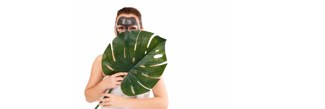 a woman with a black cosmetic mask on her face holds a green leaf in her hands.