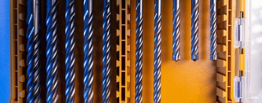 Panoramic closeup photo shot of yellow and transparent kit box with drills for drilling holes on a white table. Repair and construction concept.