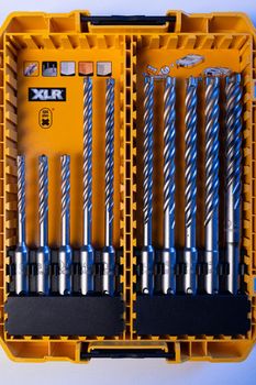 Vertical Close-up photo of yellow and transparent kit box with drills for drilling holes on a white table. Repair and construction concept.
