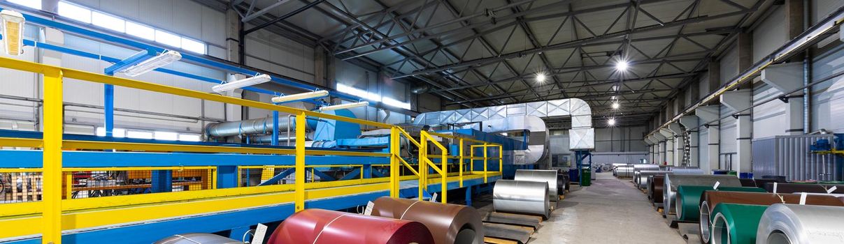 Panoramic photo shot of roll of painted galvanized steel sheet at cutting machine, ironworks and metalwork in factory. Plant concept.