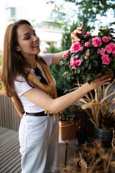 Vertical photo shot of beautiful attractive positive happy smiling young brunette woman in casual stylish look buys flowers in the store in the city.