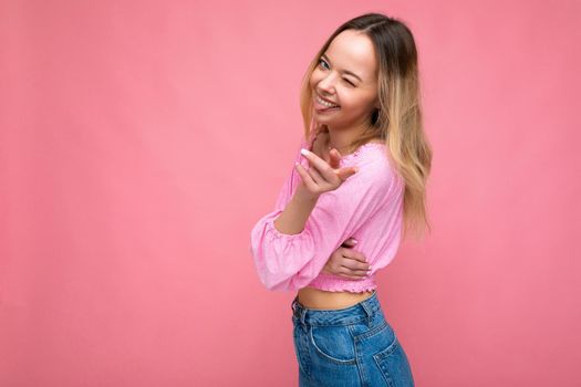 Photo shot of young beautiful cute happy blonde woman wearing stylish pink crop top isolated over pink background with copy space.