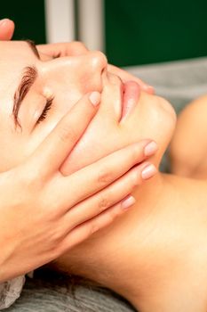 Beautiful young caucasian woman with closed eyes receiving a facial massage in a beauty salon