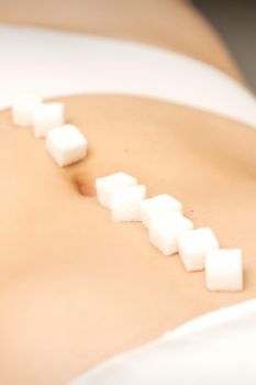 The concept of epilation, waxing. Sugar cubes lying in a row on the abdomen of a young white woman, close up