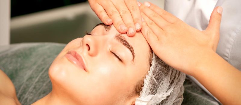 Head massage. Beautiful caucasian young white woman receiving a head and forehead massage with closed eyes in a spa salon