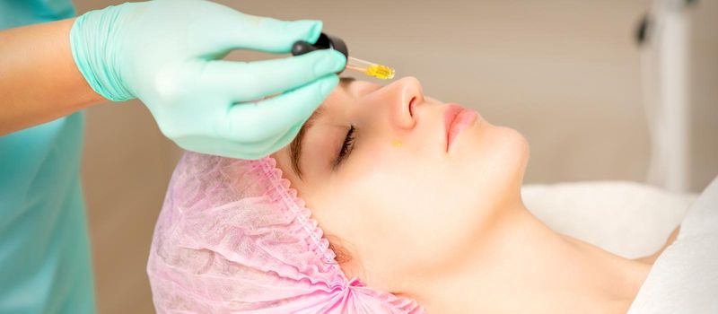 Young white woman getting acid organic retinol peel face skin with the pipette in a beauty clinic