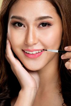 Close up young ardent woman with healthy fair skin applying lipstick on her lip while looking at camera. Beauty concept with cosmetic and makeup.