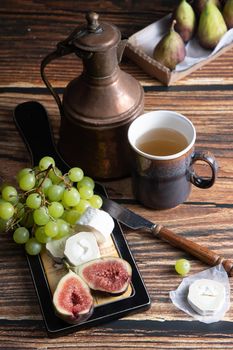 cheese plate with goat cheese, grapes and figs, copper teapot, angle view, healthy food, high-calorie breakfast. High quality photo