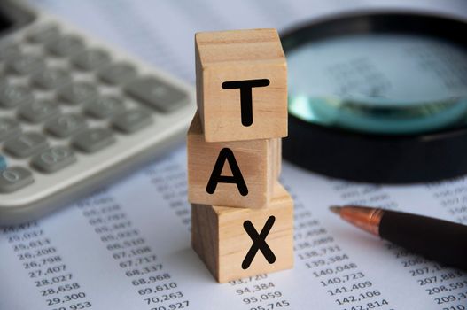 Tax word on wooden blocks with calculator, pen, magnifying glass and data analysis background. Tax concept.