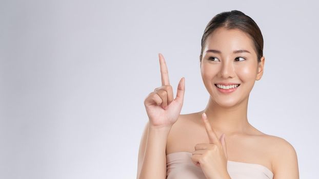 Photo of a gorgeous woman in a concept of empty space for beauty care product on isolated light gray background. Skincare product, model uses hand to create empty space for commercial.