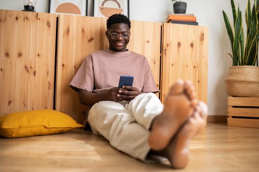 Young african american man relaxing at home using mobile phone browsing through social media. Lifestyle.