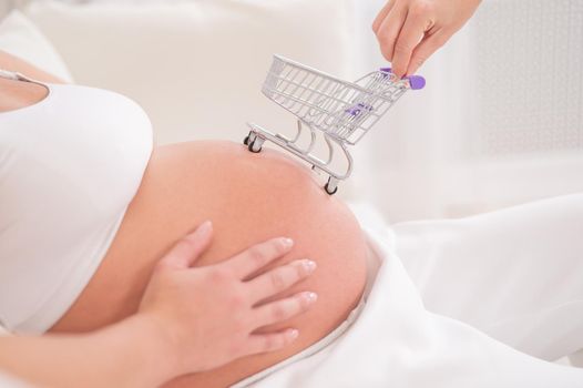 Faceless pregnant woman with shopping cart on her belly