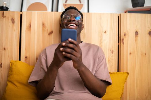 Young black man laughing at home relaxing using mobile phone to watch funny videos. Reading text message. Lifestyle