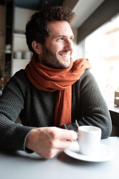 Vertical portrait of happy man having morning coffee in coffee shop looking out the window. Lifestyle concept.