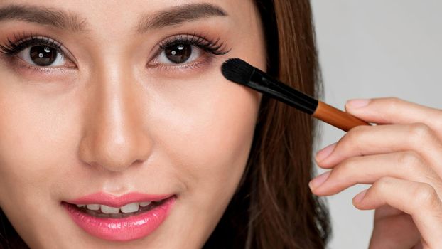 Closeup ardent young woman with healthy fair skin applying her eyeshadow with brush. Female model with fashion makeup. Beauty and makeup concept.