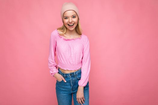 Photo of beautiful happy smiling joyful young blonde woman isolated over pink background wall wearing trendy pink hat and pink blouse looking at camera.