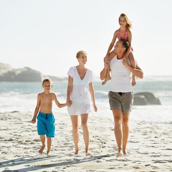 Hitching a ride on the dad-mobile. A happy young family walking down the beach together in the sunshine