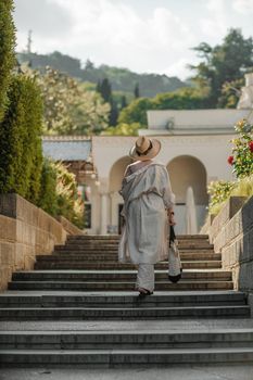 Woman on the stairs in the park. A middle-aged lady in a hat in a white outfit with a bag walks around the Livadia Palace.