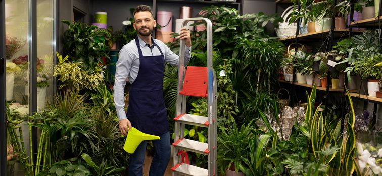 florist with a watering can in his hands and a stepladder on the background of a flower shop.