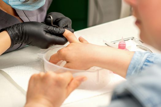 Manicure master removes cuticles from female nails with scissors wearing protective gloves in manicure salon