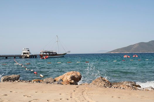 Bodrum - nice view of the sea. Beach Bodrum with sand and mountains, the sea with the ship. Beautiful harbor near the sandy beach.