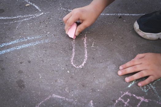 Children draw with chalk on the road. Children's creativity on the street. Entertainment in nature.