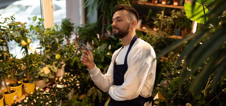 male gardener with pruning shears surrounded by potted plants.